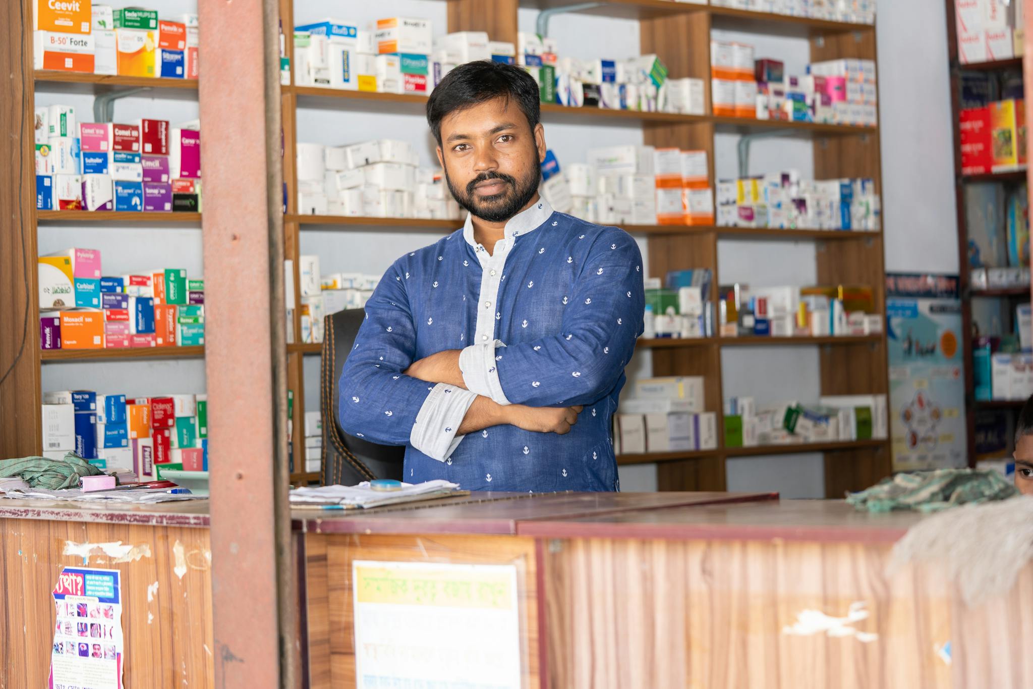 A confident pharmacist stands behind the counter of a pharmacy in Natore, Bangladesh.