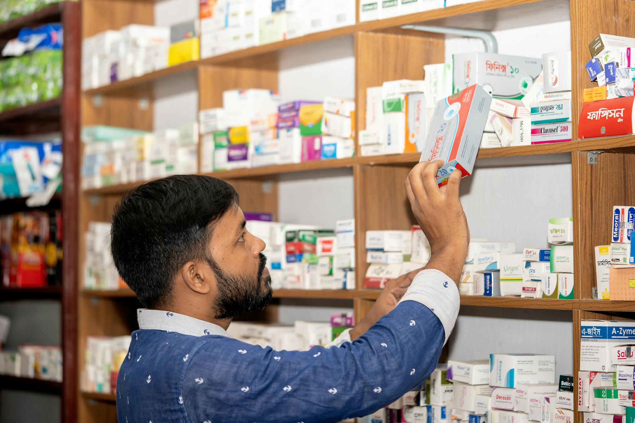 A pharmacist organizing medication on shelves in a pharmacy in Bangladesh.